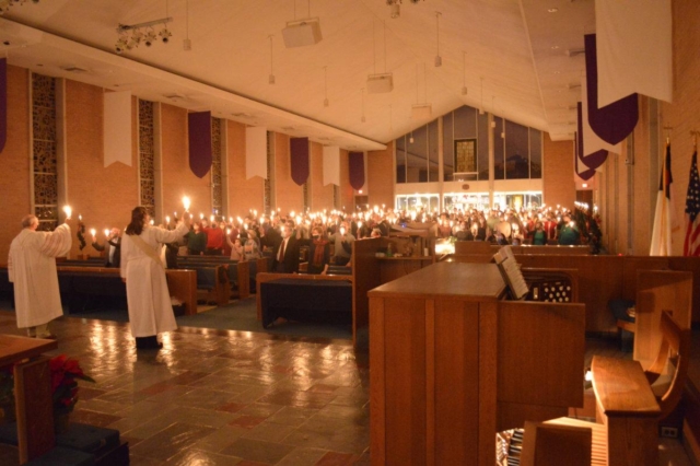 A long shot from the Chancel of the clergy and congregation holding lit candles and singing Silent Night