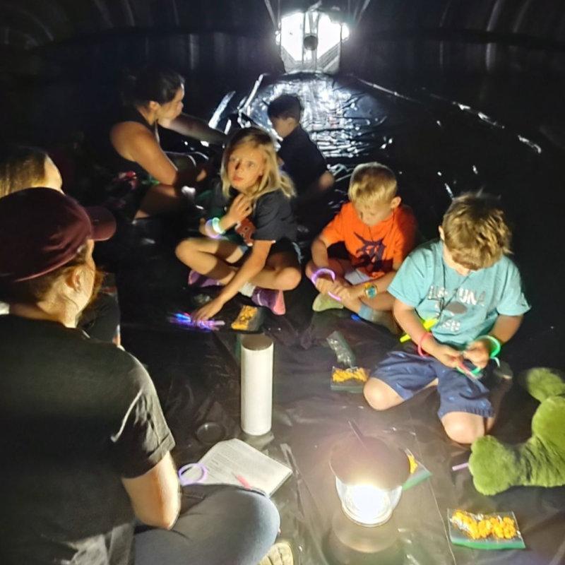 A group of kids sitting in a dark setting with a lantern hearing the story of Jonah and the Whale